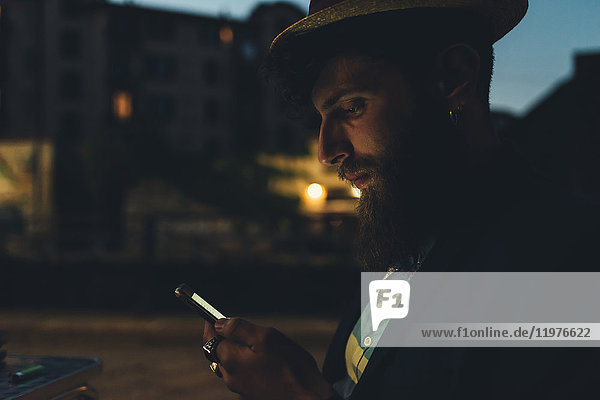 Mann auf der Straße schaut nachts auf Smartphone