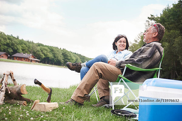 Mature couple sitting in camping chairs beside lake