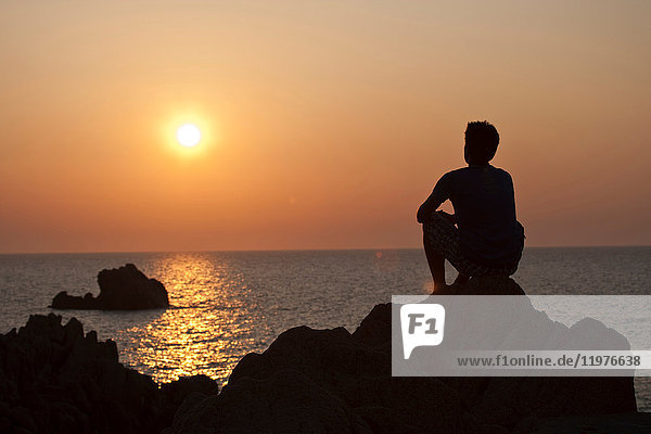 Silhouette eines Mannes auf Felsen  der den Sonnenuntergang über dem Meer betrachtet  Olbia  Sardinien  Italien