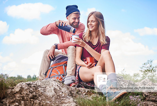 Couple hiking  sitting on rocks pouring drink from flask into enamel mug  Krakow  Malopolskie  Poland  Europe