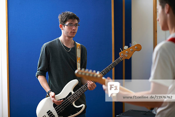 Young male college students playing guitars in recording studio