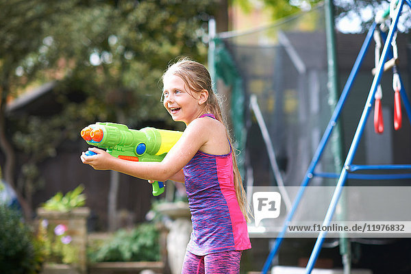 Mädchen mit nassem Haar hält Wasserpistole im Garten