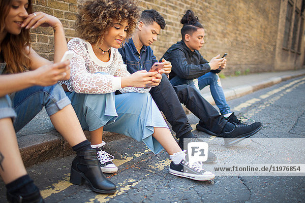 Four friends sitting in street  looking at smartphones