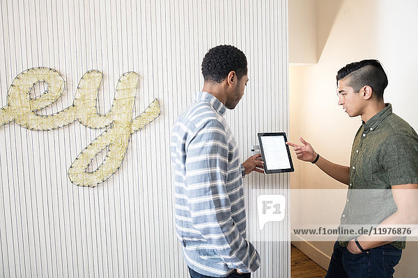 Coole junge Geschäftsleute im kreativen Büro schauen sich digitales Tablet an