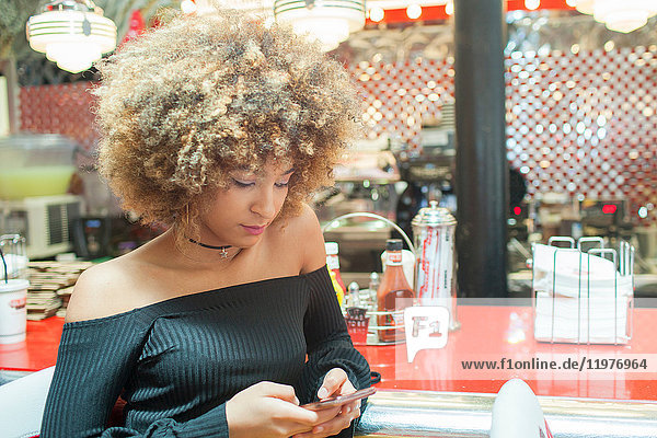 Young woman sitting in diner  looking at smartphone