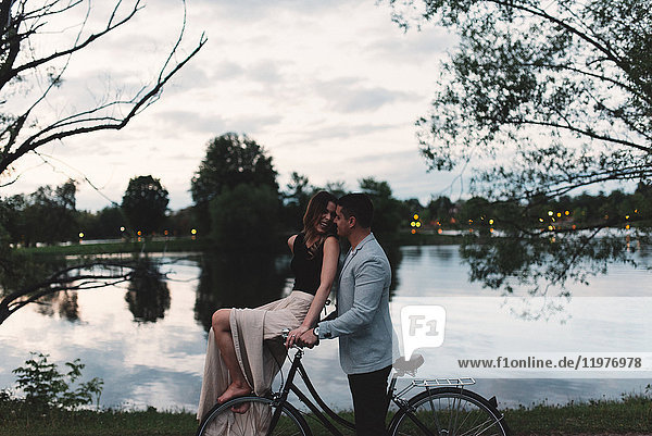 Romantisches junges Paar auf dem Fahrrad  das sich in der Abenddämmerung am See anschaut