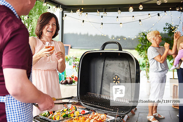 Man and woman laughing while barbecuing on patio at family lunch