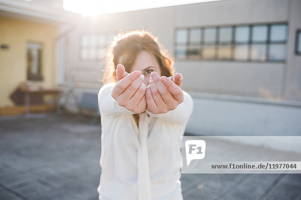 Portrait of beautiful young woman dancing with hands reaching out on sunlit roof terrace
