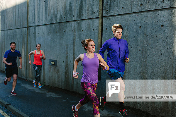 Four young adult runners running along city sidewalk