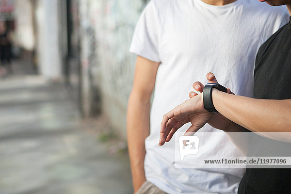 Two young men in street  looking at smartwatch  mid section