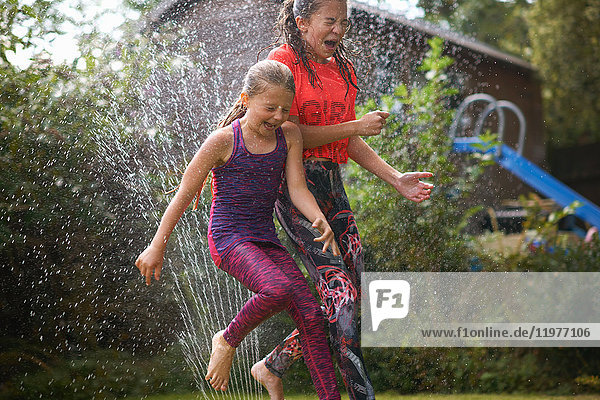 Girls jumping over garden sprinkler