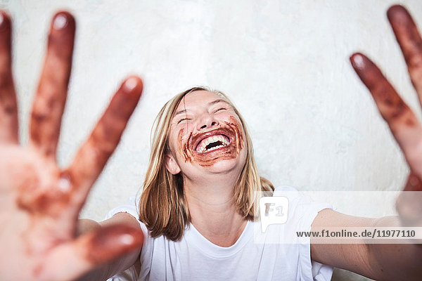 Porträt einer Frau mit Schokolade an den Händen und um den Mund  die Hände in Richtung Kamera haltend  lachend