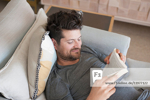 Mittelgroßer erwachsener Mann entspannt sich auf dem Sofa  liest ein Buch  erhöhter Blick