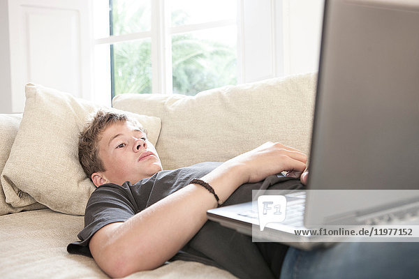Teenage boy lying on sofa looking at laptop