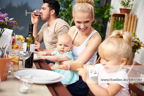 Couple with baby and toddler daughters at family lunch on patio table