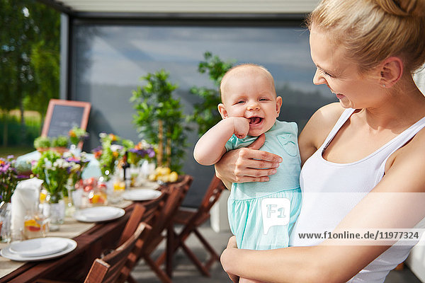 Young woman carrying baby daughter at family lunch by patio table