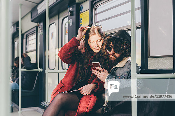 Junges Paar sitzt in der U-Bahn und schaut auf ein Smartphone