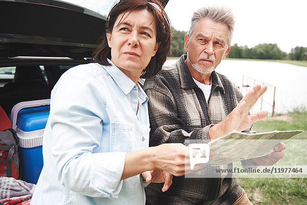 Älteres Ehepaar in ländlicher Umgebung  steht neben dem Auto und schaut auf die Karte
