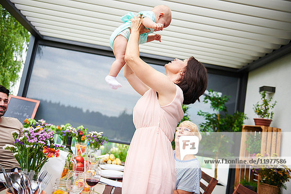 Mature woman lifting up baby granddaughter at family lunch on patio