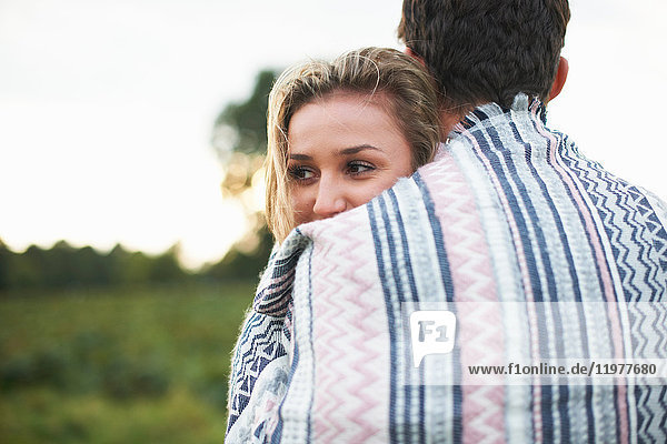 Junges Paar umarmt sich in eine Decke gehüllt im Feld