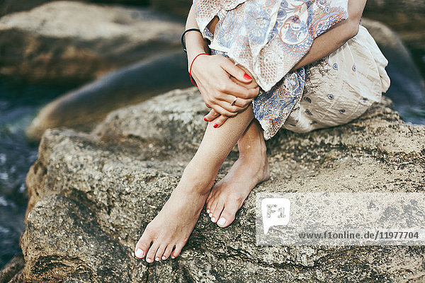 Waist down view of young woman sitting barefoot on coastal rock  Odessa  Ukraine
