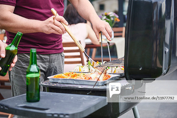 Mid section of man barbecuing on patio at family lunch