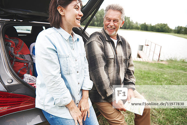 Mature couple in rural setting  standing beside car  laughing