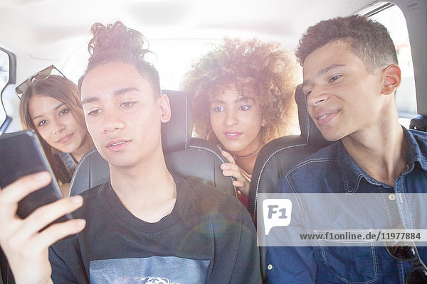 Four friends in taxi  looking at smartphone
