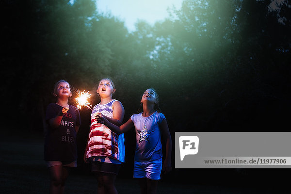 Drei Mädchen mit Wunderkerzen  die am Unabhängigkeitstag nachts aus dem Garten aufblicken  USA