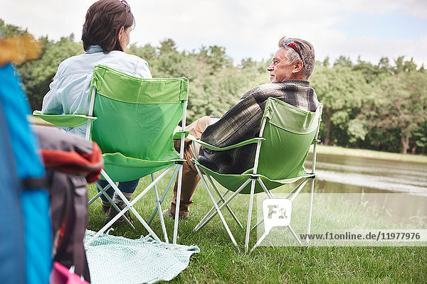Älteres Paar sitzt in Campingsesseln am See  Rückansicht