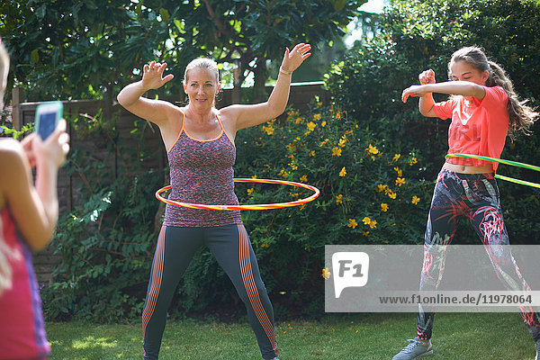 Girl photographing mother and teenage sister hoola hooping in garden