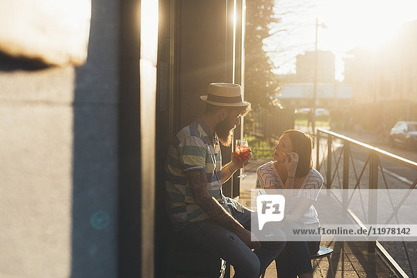 Ein Paar sitzt vor einem sonnenbeschienenen Straßencafé und trinkt Cocktails