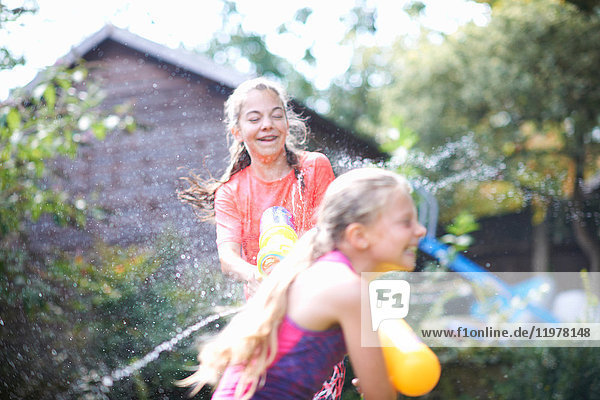 Teenager-Mädchen und ihre Schwester bespritzen sich gegenseitig im Garten mit Wasserpistolen