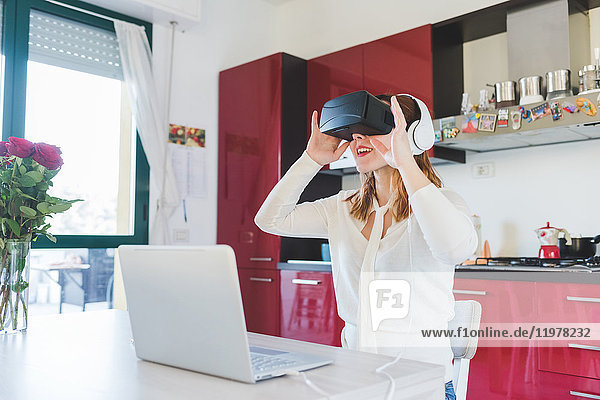 Junge Frau am Küchentisch  die durch ein Virtual-Reality-Headset blickt