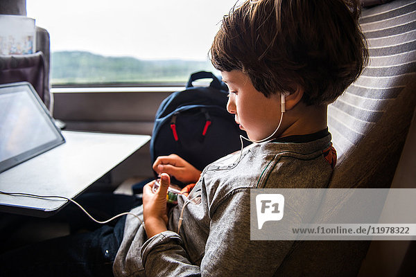 Kleiner Junge reist im Zug  benutzt ein digitales Tablet und trägt Kopfhörer