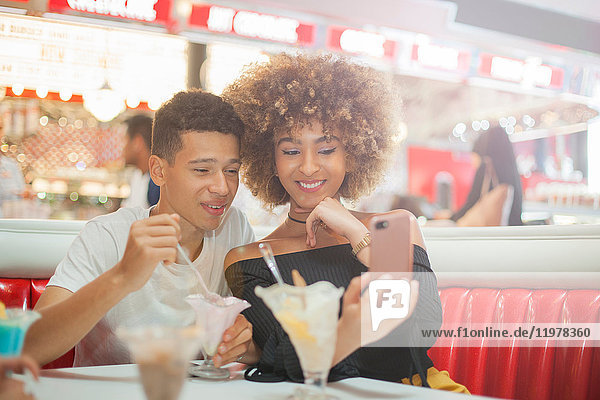 Junges Paar sitzt im Diner  schaut auf Smartphone  lacht