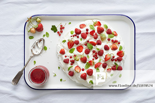 Pavlova mit roten Johannisbeeren,  Erdbeeren und frischer Minze auf Serviertablett