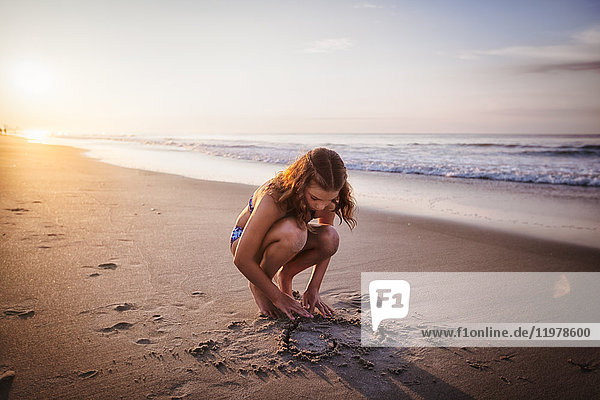 Mädchen malt Herz im Sand am Strand