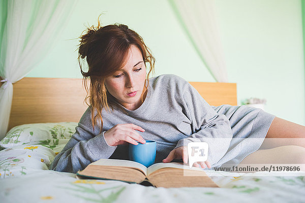 Young woman reclining on bed reading a book