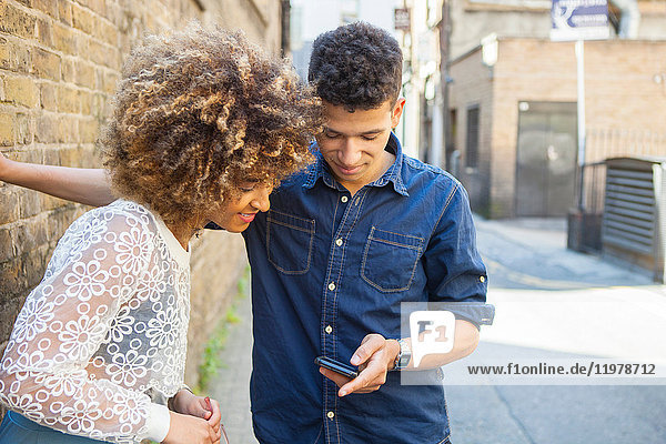 Junges Paar auf der Straße  das sich ein Smartphone ansieht