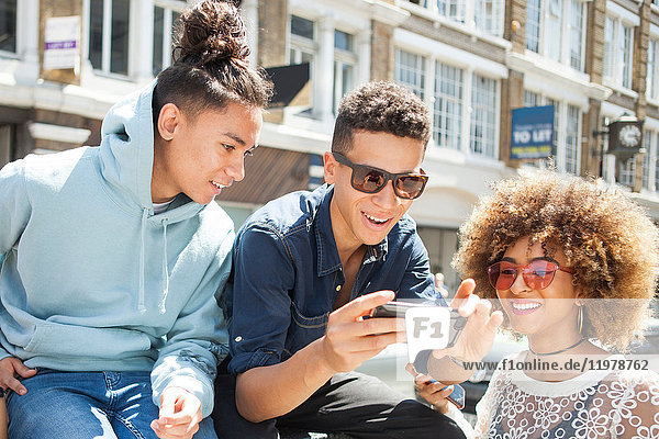 Drei junge Freunde im Freien  die sich ein Smartphone anschauen