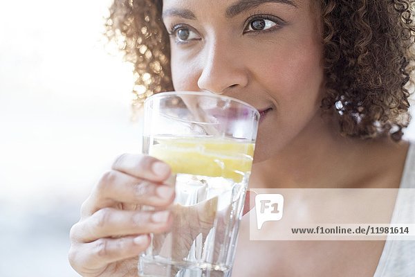 Mittlere erwachsene Frau trinkt Wasser mit einer Zitronenscheibe.