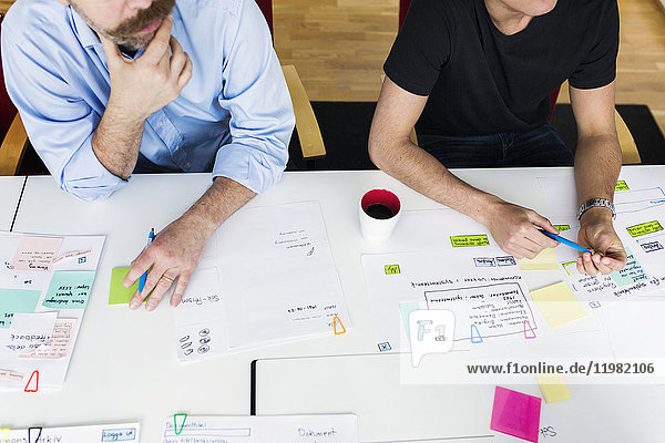 Colleagues sitting by conference table and brainstorming