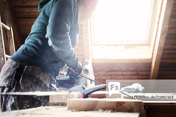 Frau benutzt Elektrowerkzeug bei der Renovierung eines alten Dachbodens