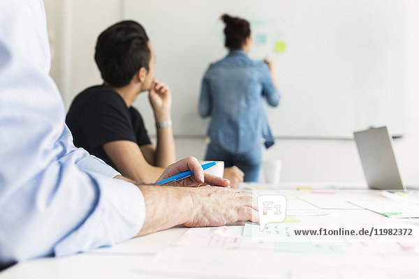 Colleagues looking at coworker writing on whiteboard