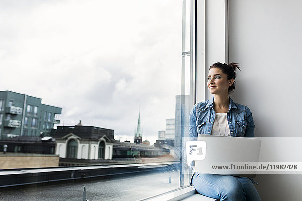 Young woman with laptop looking through window