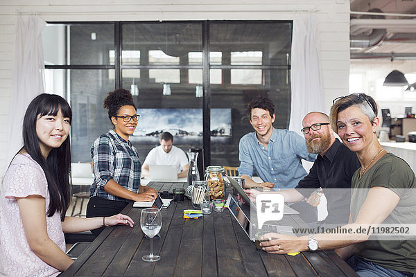 Group of coworkers looking at camera one man working in background