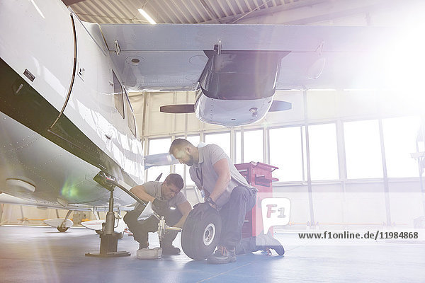 Männliche Mechaniker,  die Räder am Flugzeug im Hangar befestigen