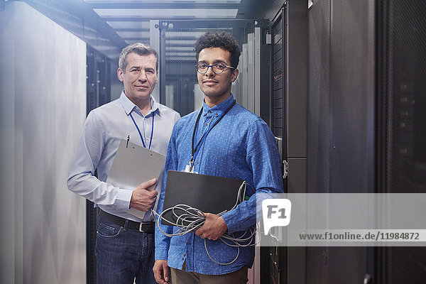 Portrait confident male IT technicians with laptop and clipboard in server room
