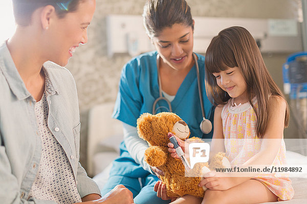 Krankenschwester und Mutter beobachten ein Mädchen  das einen Insulinstift auf einem Teddybär benutzt